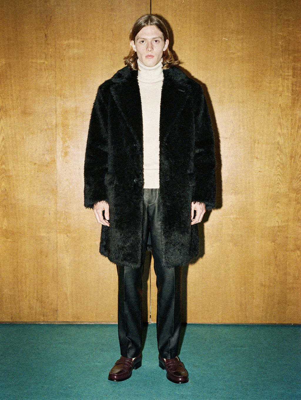 Model in a black faux-fur coat against a wood-panelled wall