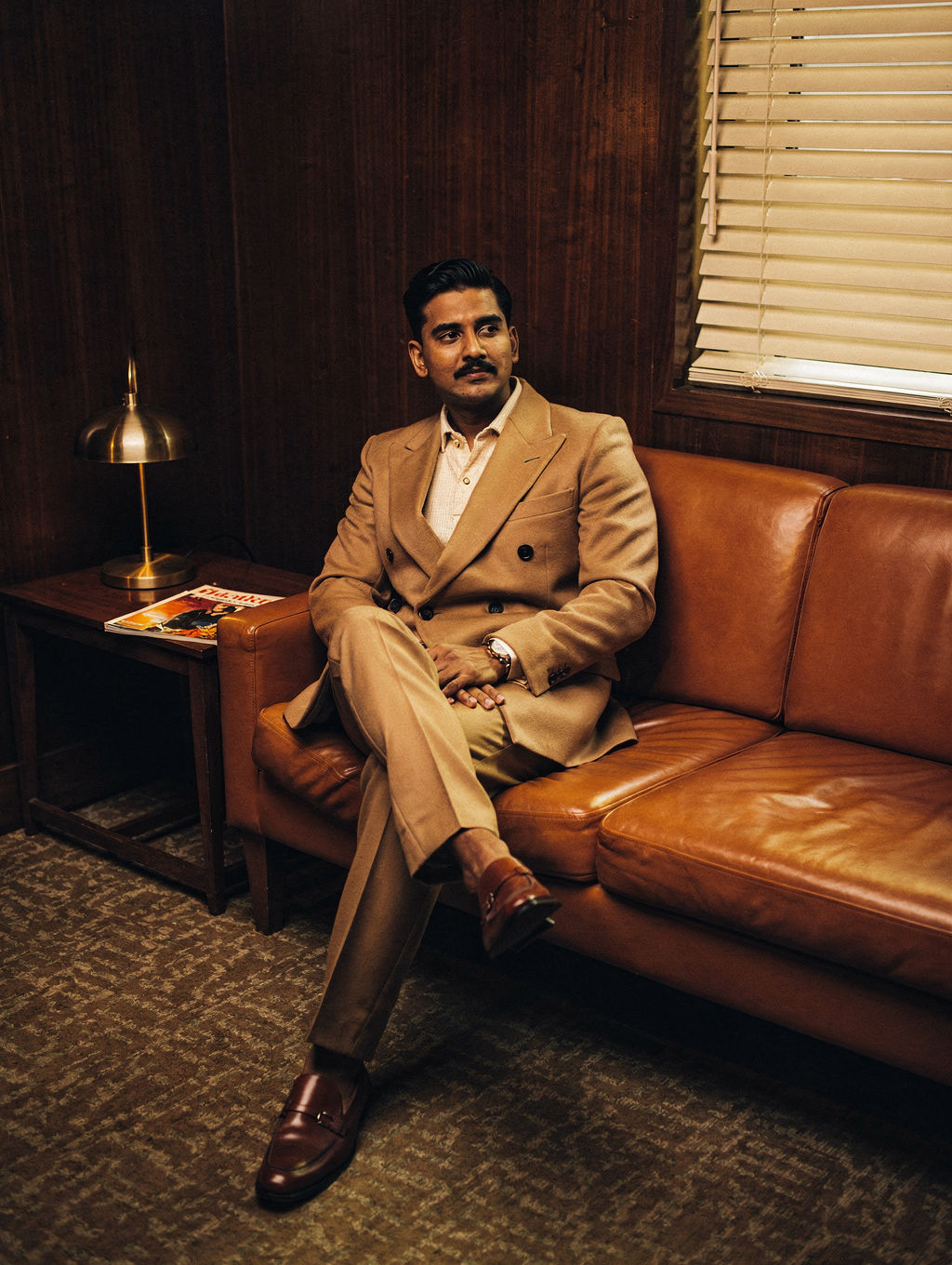 Man in a camel double-breasted suit on a burnt-orange leather banquette