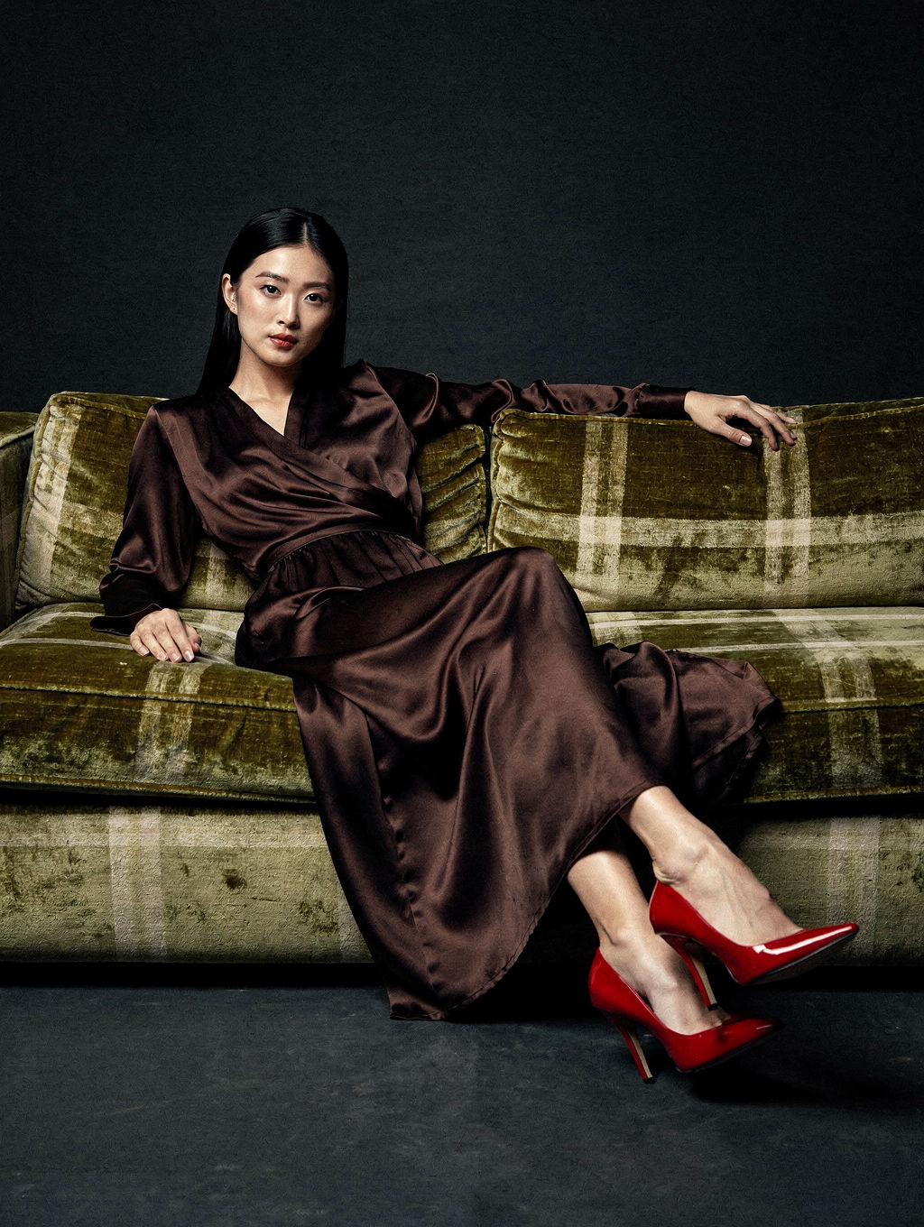 Model reclining on a checked velvet sofa in a brown silk dress