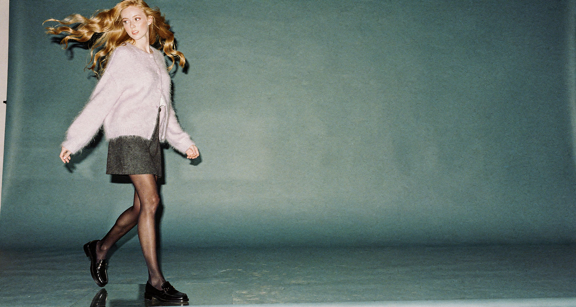 Model mid-stride in a lilac mohair cardigan against slate-blue paper