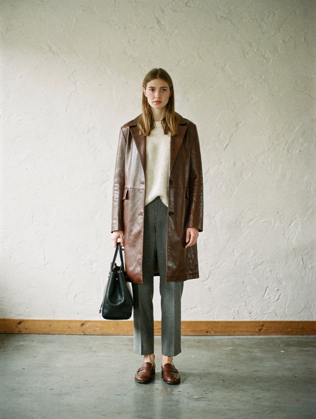Model in a chocolate leather coat against a plain plaster wall