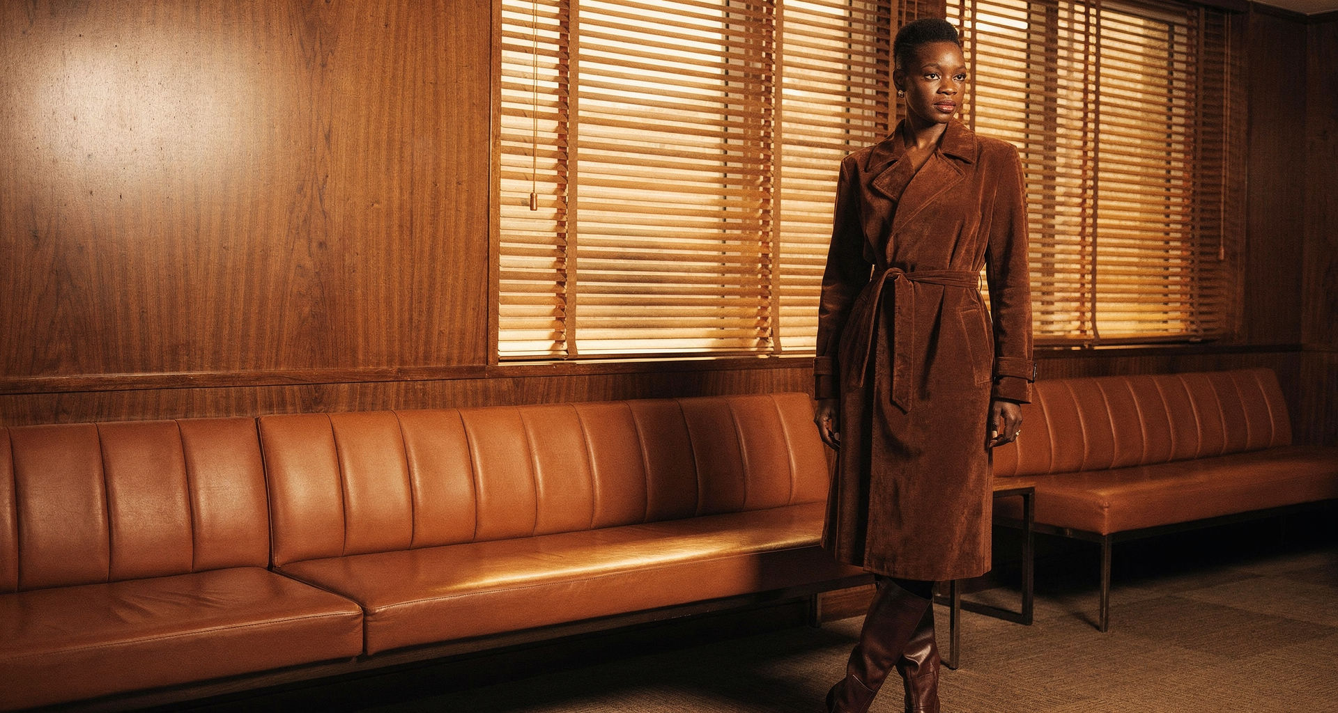 Model in a chocolate suede trench coat in a walnut-panelled lounge