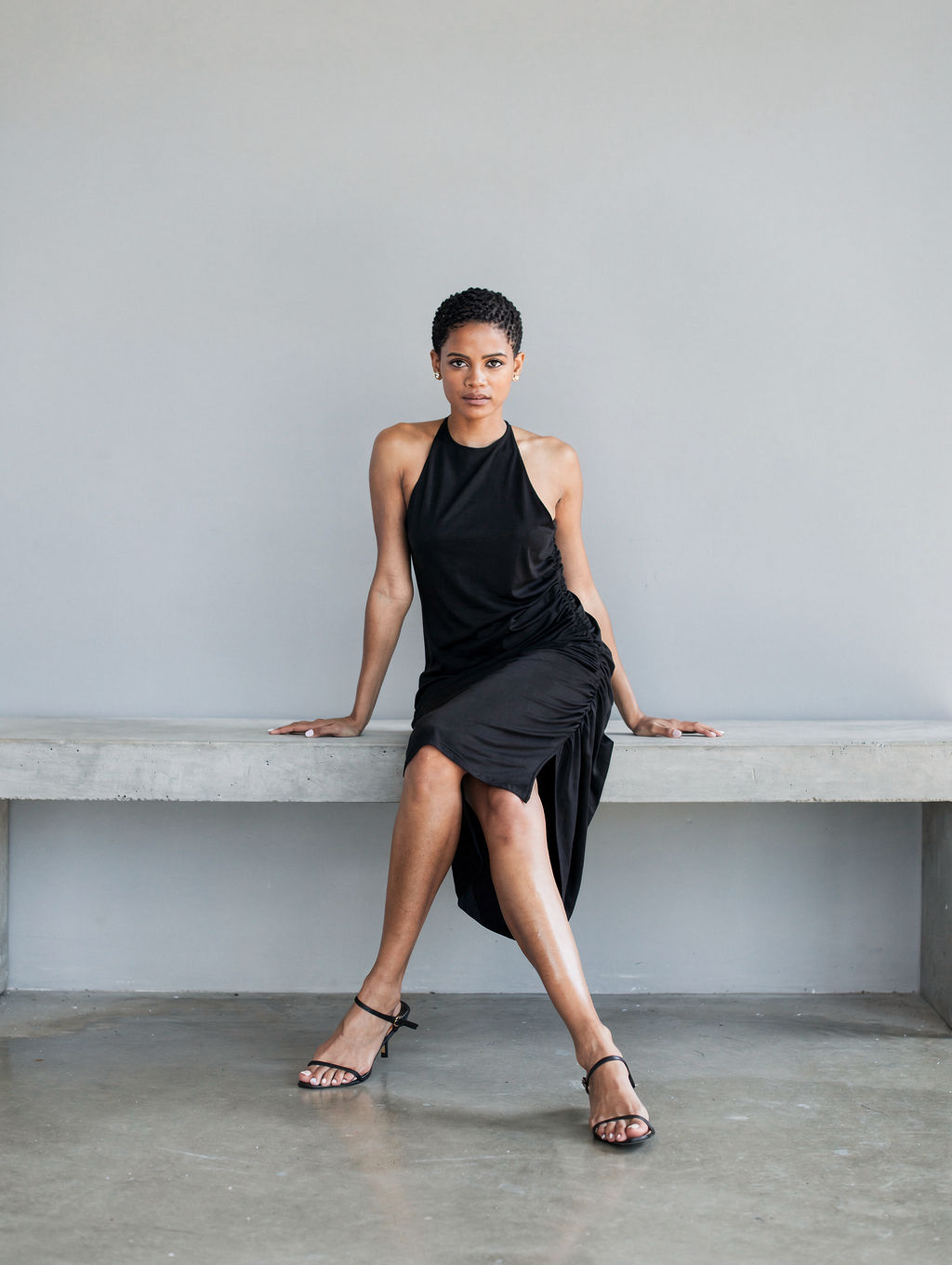 Model in a black jersey halter dress on a concrete bench