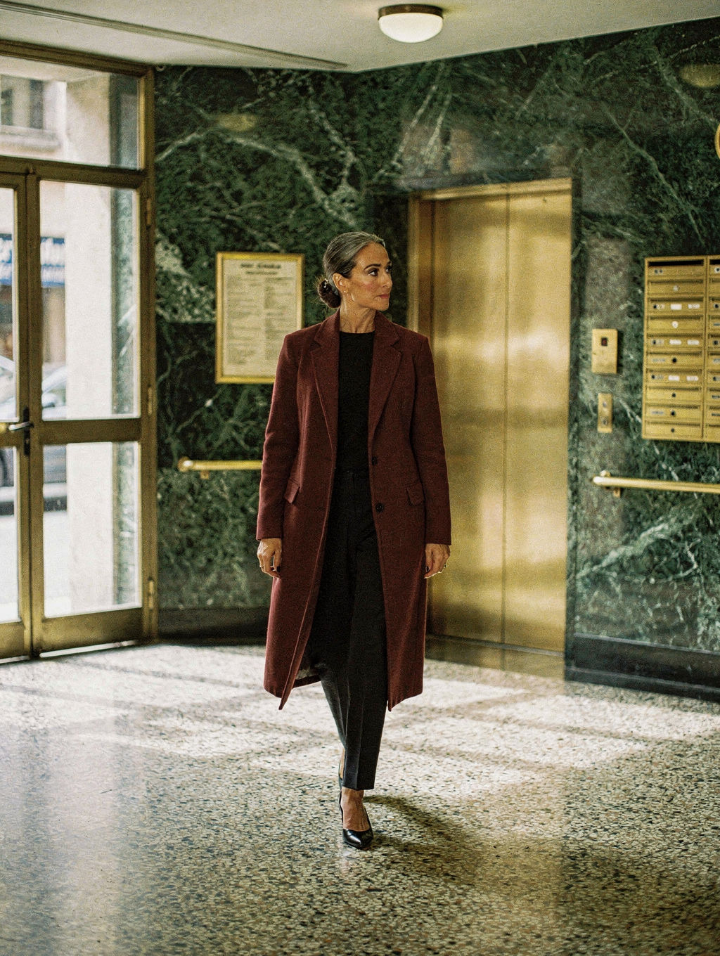 Woman in a long oxblood coat crossing a terrazzo lobby
