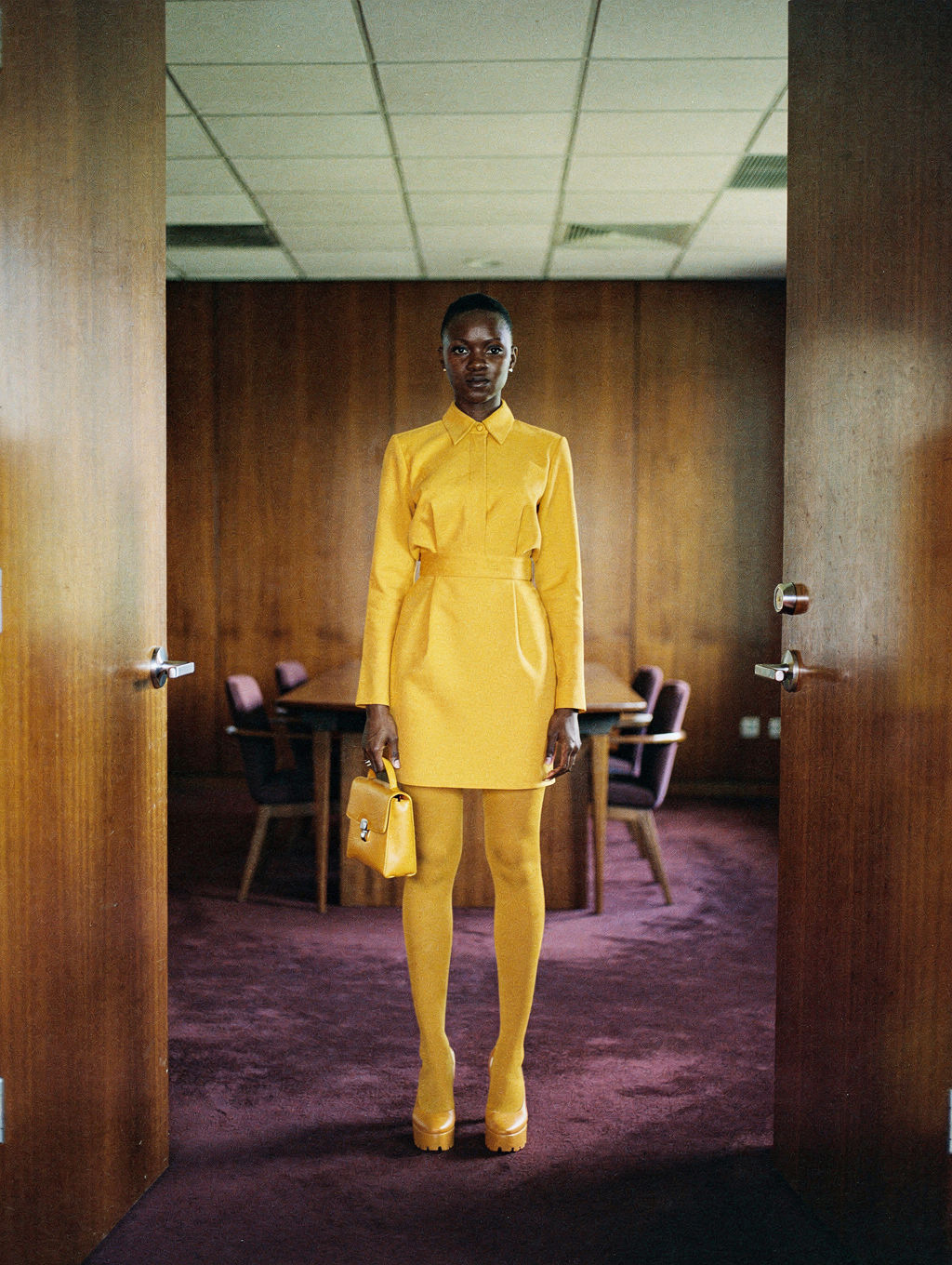 Model in a saffron shirt dress framed by open walnut doors